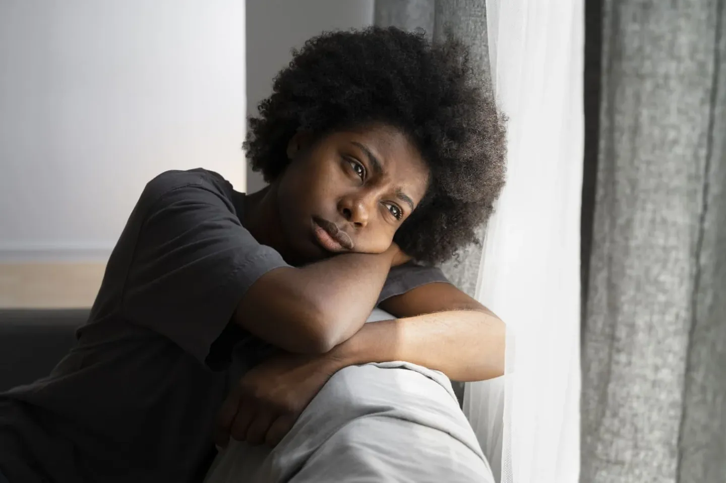 Jovem com semblante triste apoiada no sofá, sinal de depressão