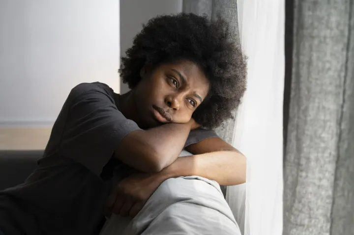 Jovem com semblante triste apoiada no sofá, sinal de depressão